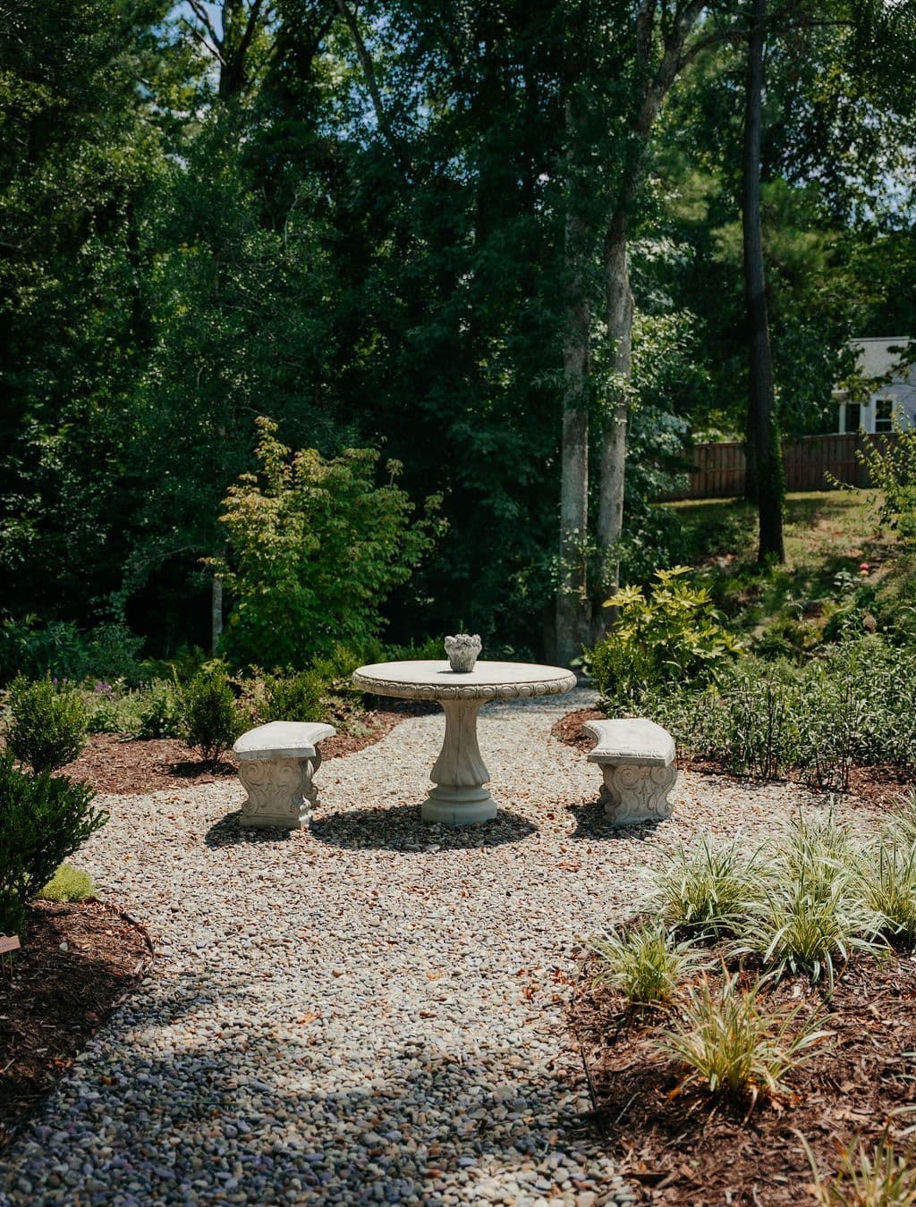A stone table and benches tucked into a shaded gravel nook.