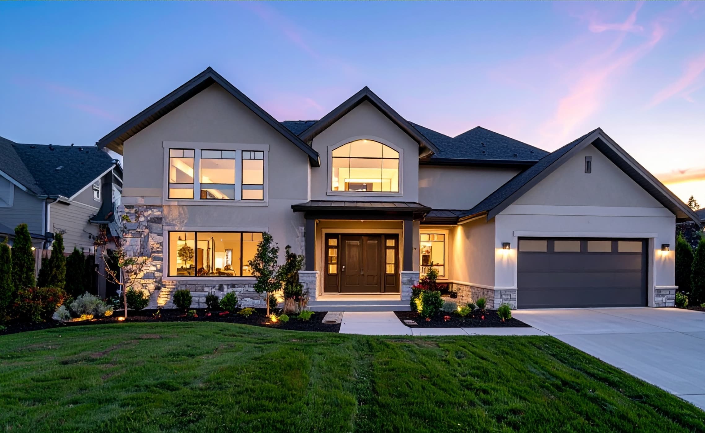 A two-story home with landscape lighting glowing at dusk.