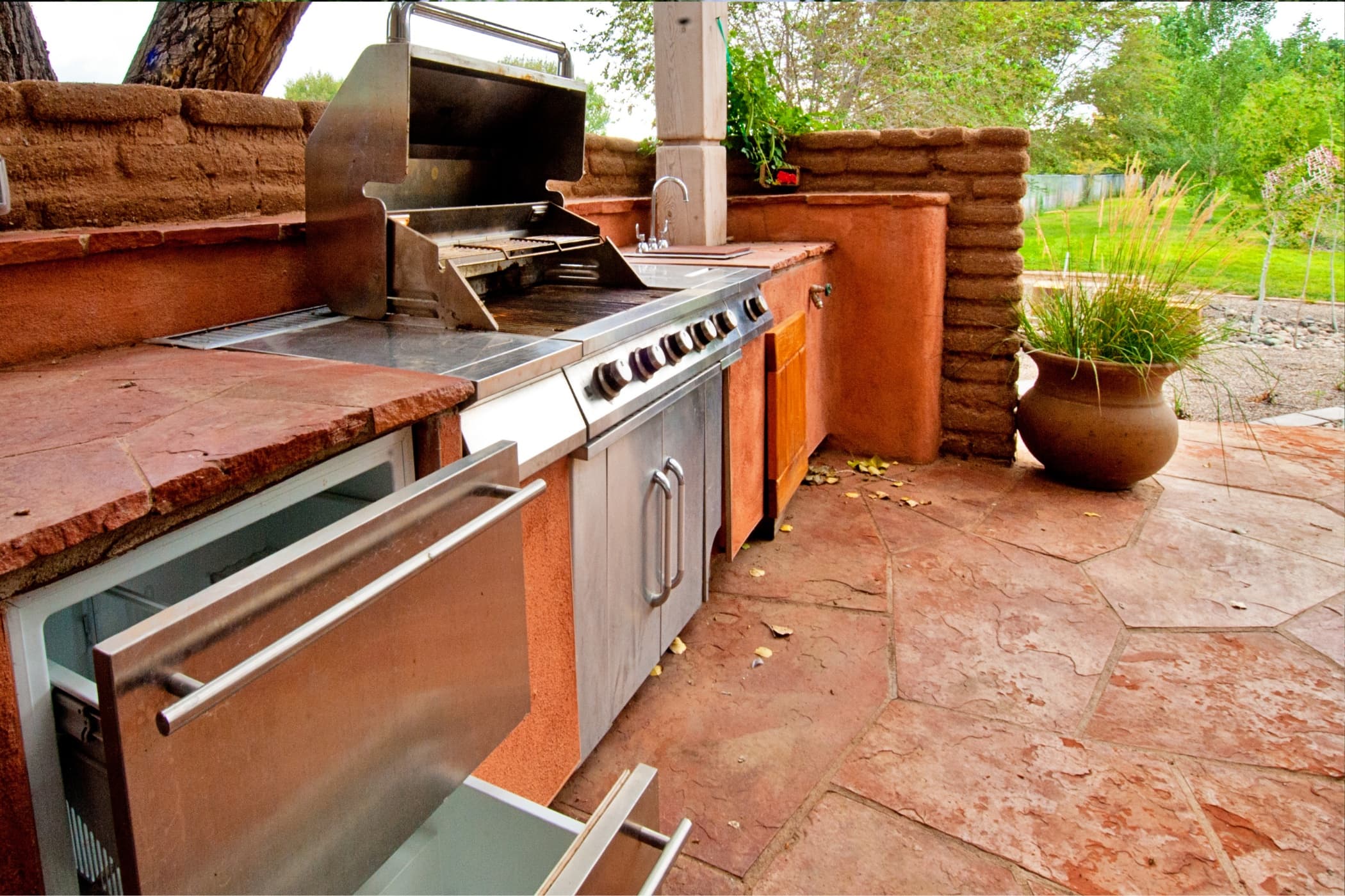 A built-in outdoor kitchen with a stainless grill, sink, and stone counters.