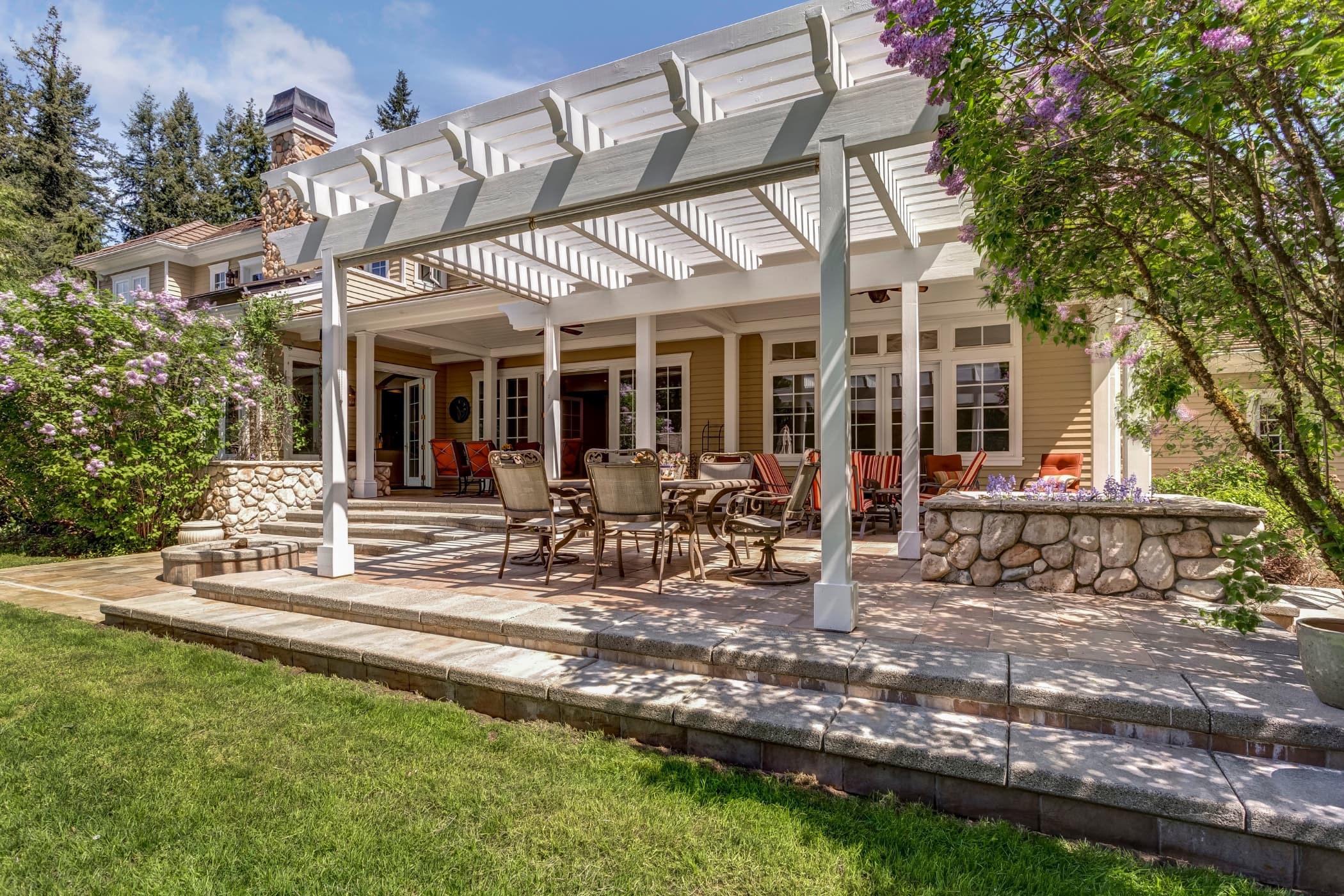 A white pergola shading a stone patio with dining and lounge seating.