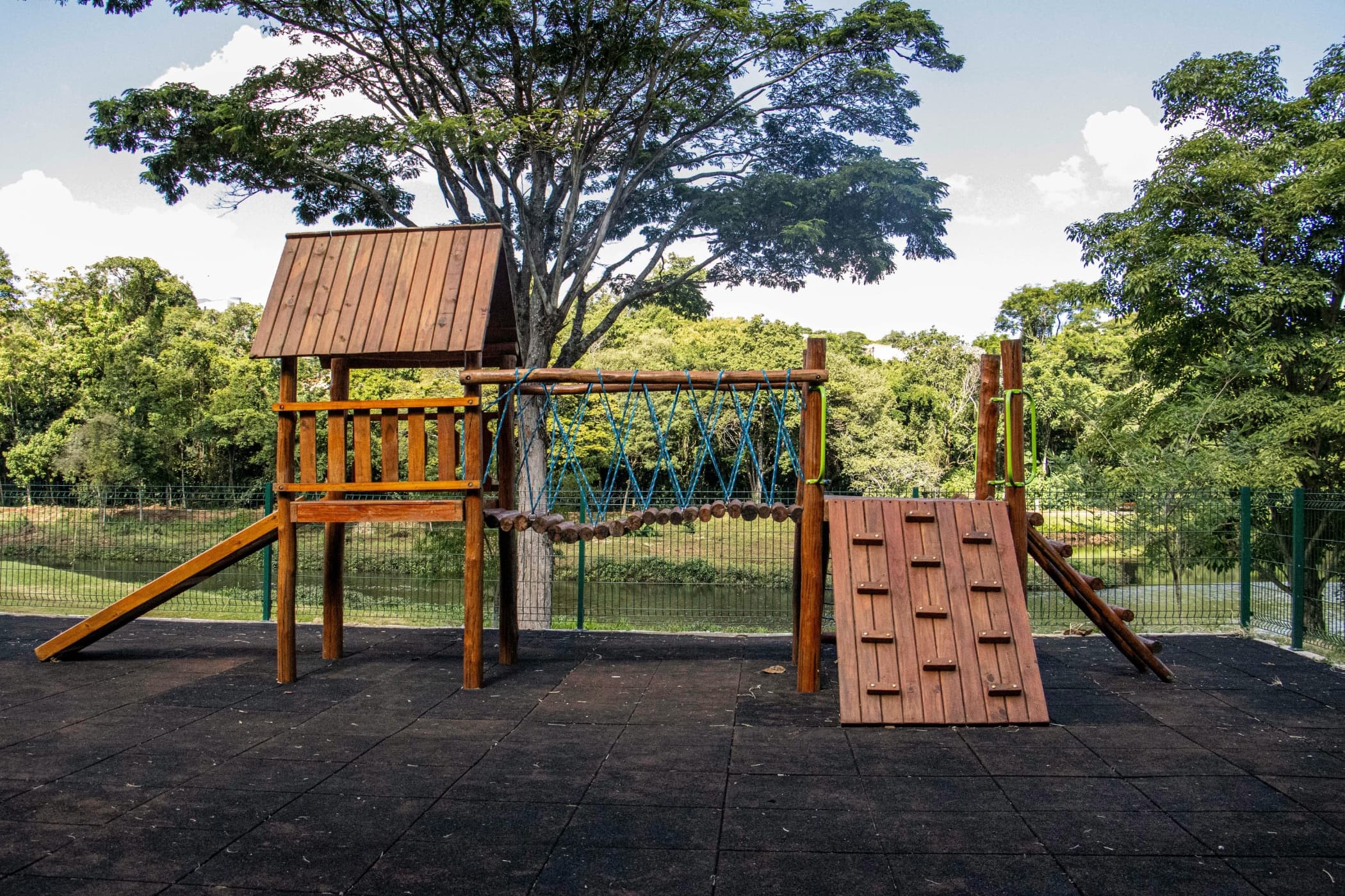 A wooden playset with a slide, climbing wall, and rope bridge.